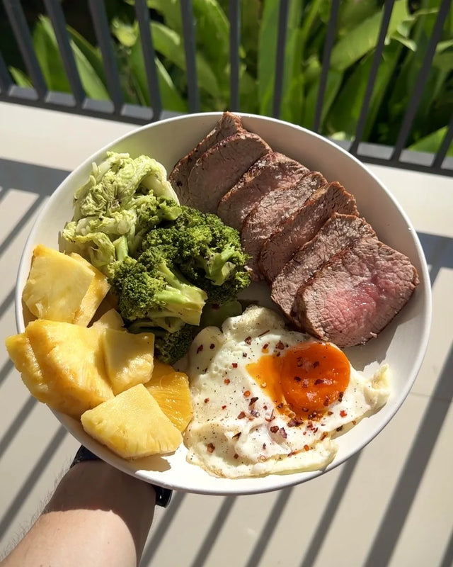 A steak and egg plate with broccoli and pineapple, held on a balcony