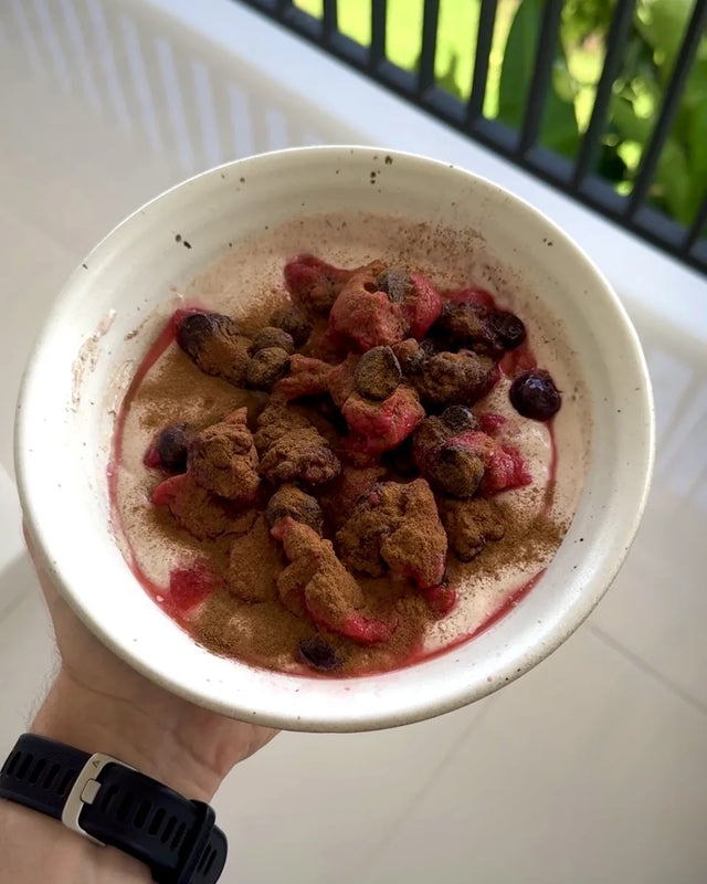 A bowl with yoghurt, berries and cinnamon, held on a balcony