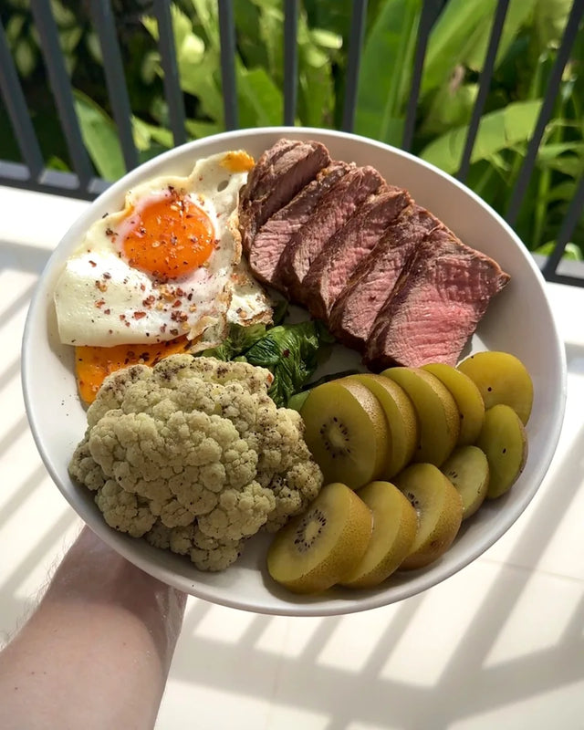 A steak and egg plate with cauliflower and kiwi, held on a balcony